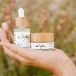 Close-up of hand holding natural skincare products, featuring serum and cream in eco-friendly packaging.